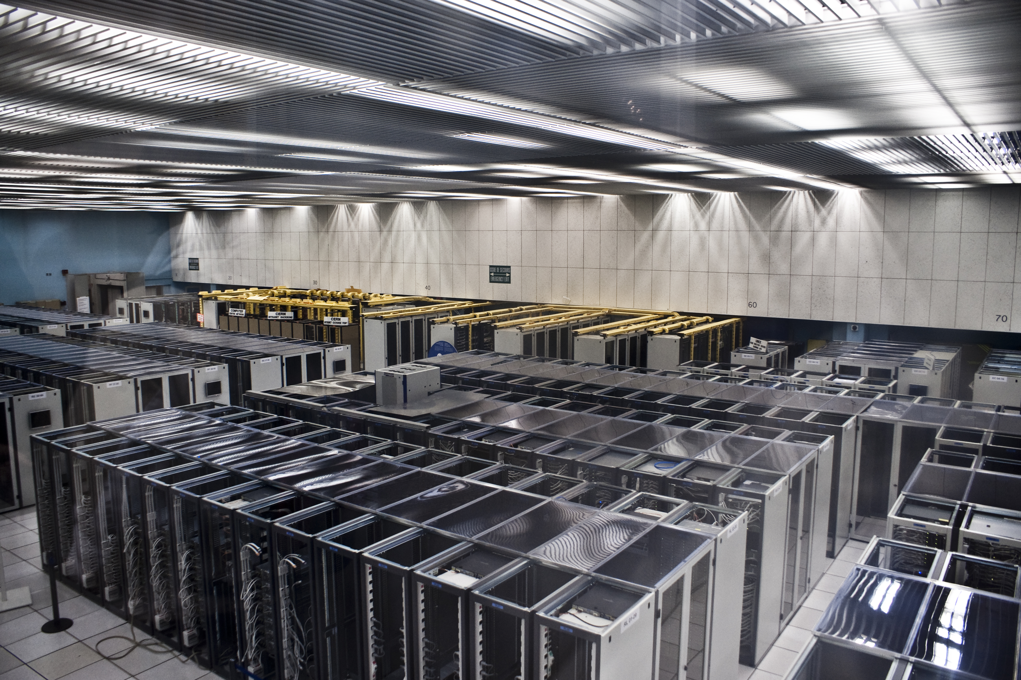 The CERN data centre: rows of enclosed racks with hot/cold aisle containment, CRAC units along the back wall, raised floor, overhead cable trays. Classic enterprise design, refined over 30 years. Photo: Florian Hirzinger, CC BY-SA 3.0